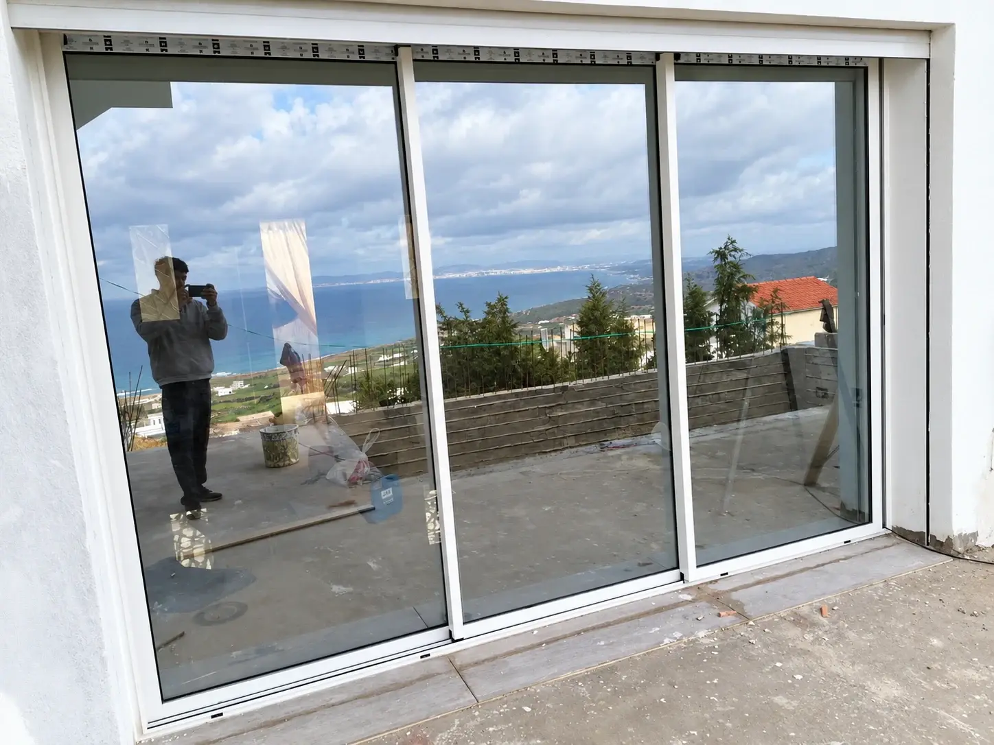 Porte-fenêtre coulissante en aluminium blanc à trois vantaux, vue depuis la terrasse avec le reflet de la mer