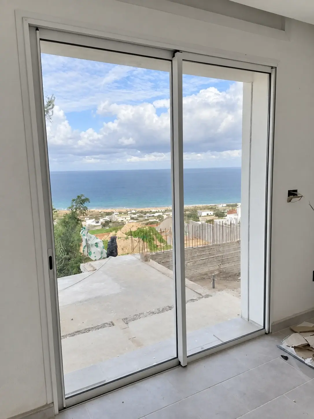 Porte-fenêtre coulissante en aluminium blanc à deux vantaux, ouvrant sur une terrasse avec vue sur la mer