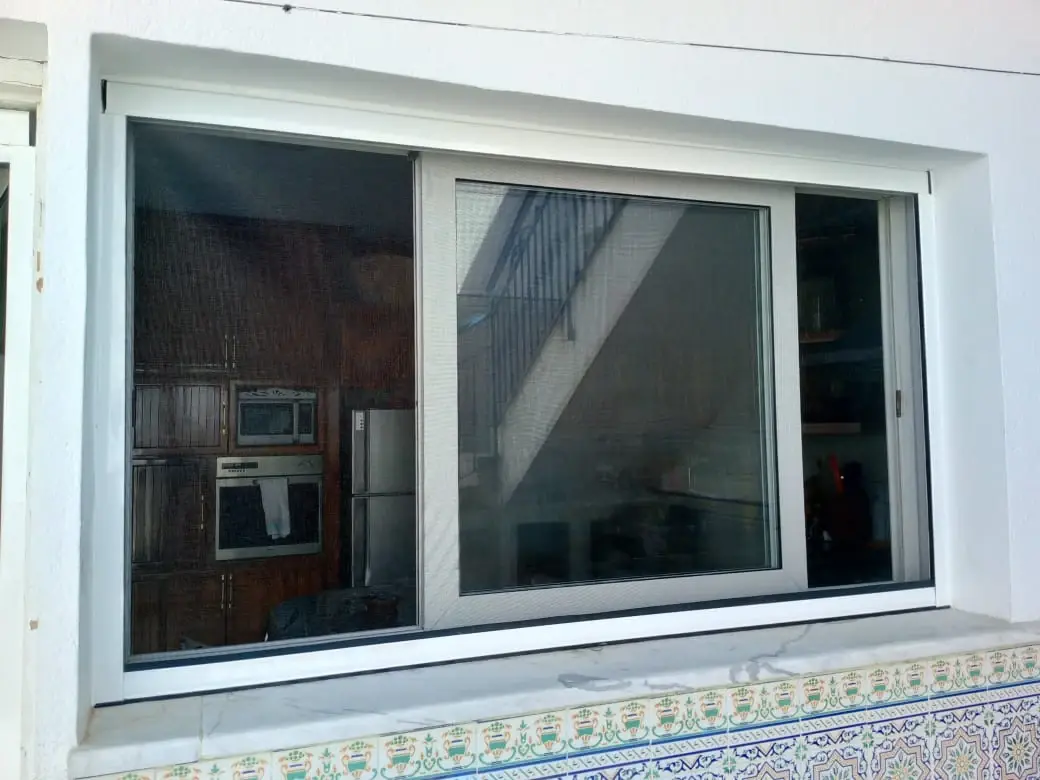Moustiquaire en aluminium blanc installée sur une fenêtre coulissante, au-dessus d'un rebord carrelé