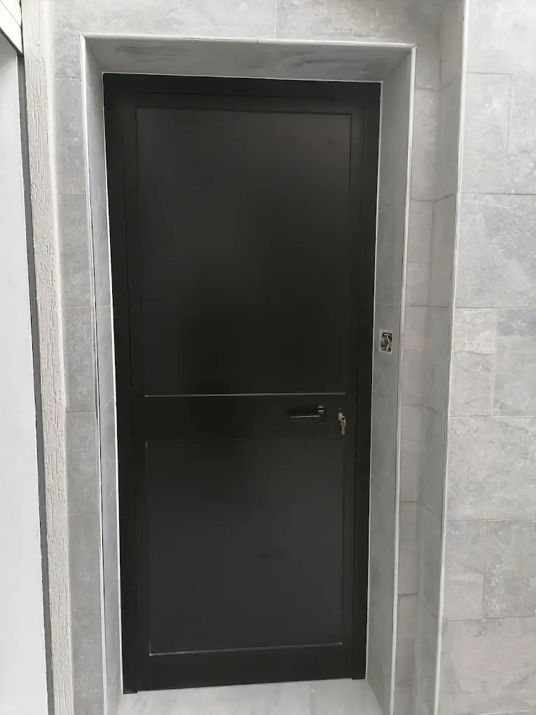 Porte en aluminium noir à deux panneaux pleins, avec poignée et serrure, dans un encadrement en pierre grise