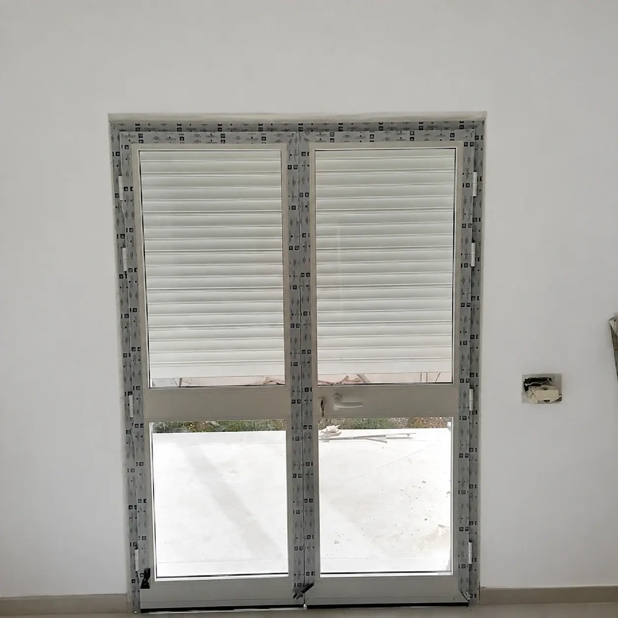 Porte-fenêtre en aluminium blanc à deux vantaux vitrés, encore protégée par son film de pose