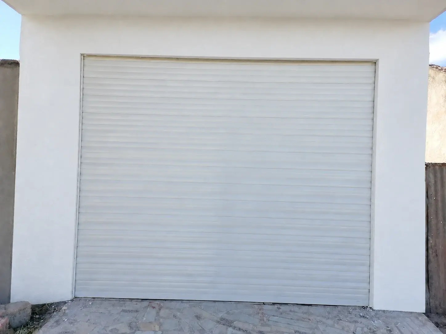 Volet roulant en aluminium blanc fermant l'ouverture d'un garage sur une façade blanche