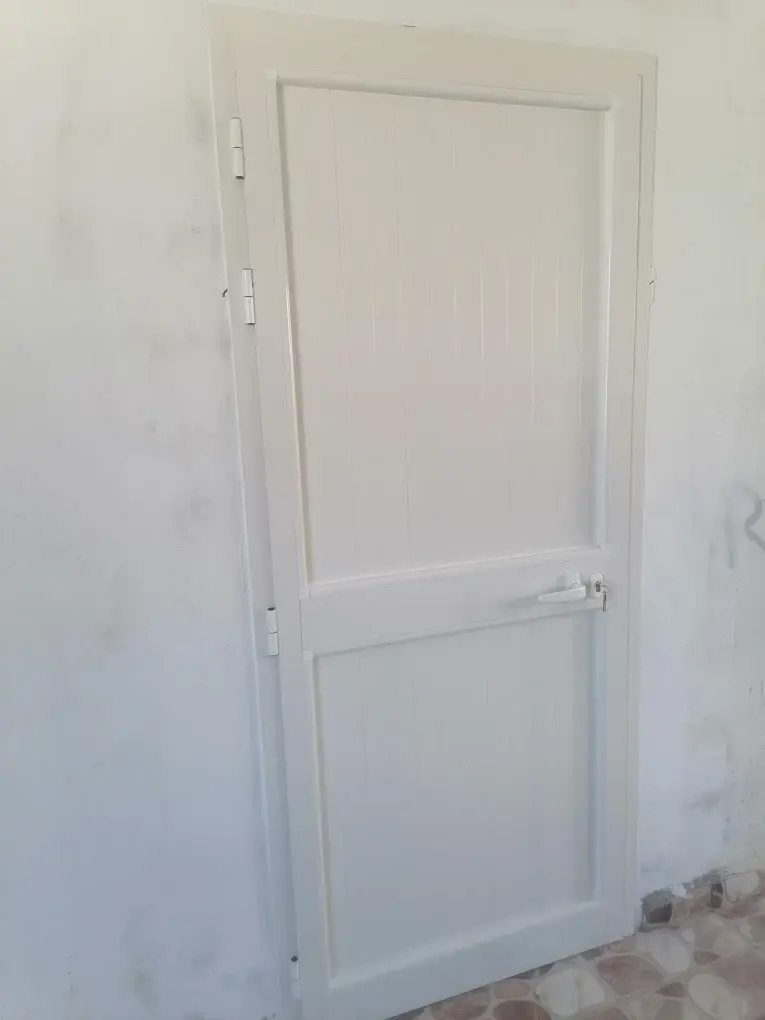 Porte de service en aluminium blanc à panneaux rainurés, avec poignée et serrure à clé