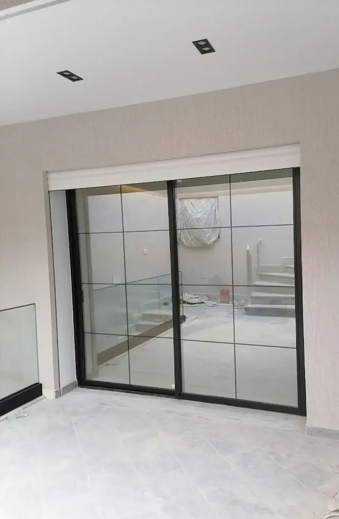 Porte vitrée coulissante en aluminium noir à petits-bois, avec un garde-corps en verre visible à gauche